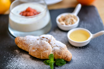 croissant with jam and sweets on black slate sprinkled with powdered sugar