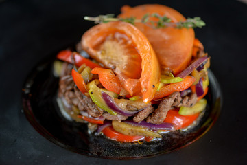 warm salad with veal decorated with slices of tomatoes on a black round plate