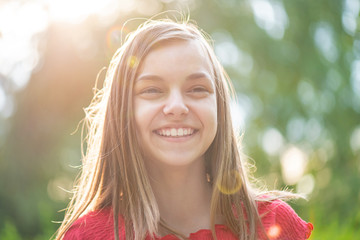 Close up portrait of teenage girl with sun rays filtering through her hair. Happy smiling teen at summer park in flare sunshine. Child looking away during sunset. - 282245354