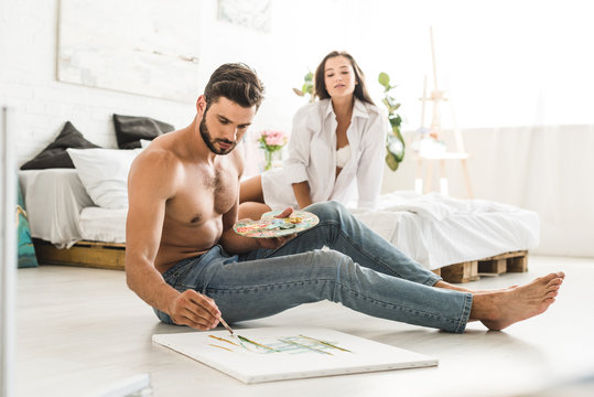 selective focus of couple sitting in bedroom while man drawing and girl looking at guy