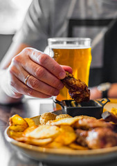 man hand with glass of cold beer and plate with snacks on wooden table background on bar or pub