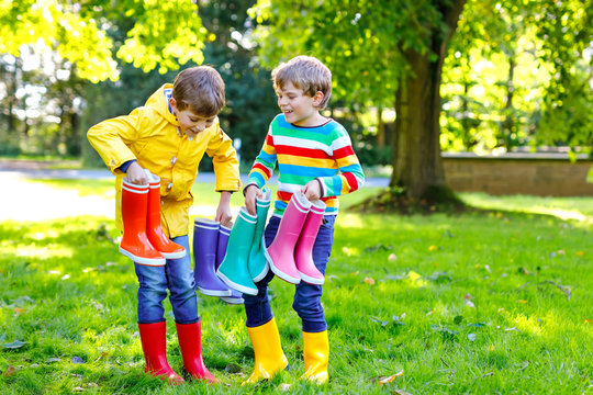 Two little kids boys, cute siblings with lots of colorful rain boots. Children in different rubber boots and jackets. Footwear for rainy fall. Healthy twins and best friends having fun outdoors