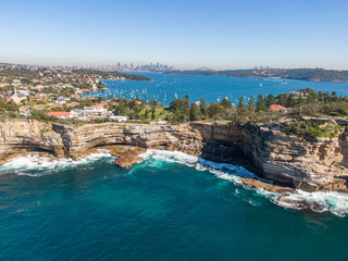 Fototapeta premium Beautiful aerial drone view of the Gap, an ocean cliff on the South Head peninsula in the suburb of Watson's Bay in eastern Sydney. The central business district of Sydney, Australia in background.