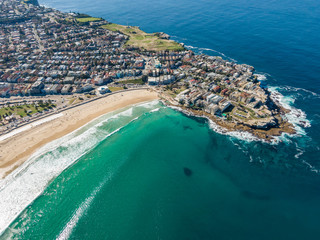 Beautiful aerial high angle drone view of the suburbs of Bondi Beach and North Bondi, one of the most famous beaches in Sydney, New South Wales, Australia. Large shoal of fish visible in the ocean.