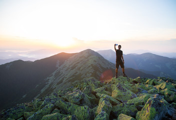 caucasian man hiker is on the peak of green stones mountain is making selfie photos on the sunset with a smartphone