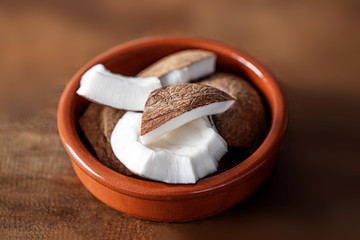 Pieces of coconut in a ceramic bowl on wooden background, top view. Coconut chunks