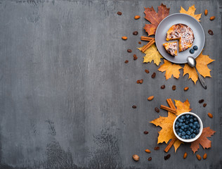 Seasonal autumn background. Frame of colorful maple leaves and a cup of hot drink, coffee, latte or cappuccino, nutmeg, cake, blueberries and cinnamon over grey.