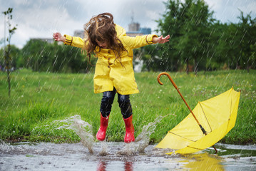 Happy child girl with an umbrella and rubber boots in puddle  jump