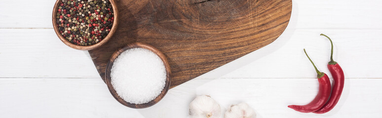 panoramic shot of wooden chopping board, garlics, salt, spices and chili peppers