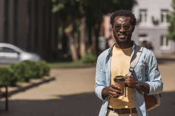 handsome, stylish african american man in glasses holding paper cup while looking at camera