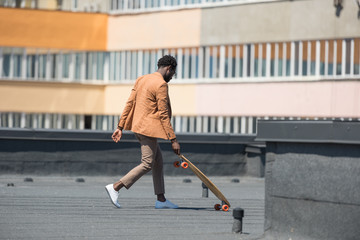 african american businessman in stylish casual clothes walking on rooftop with longboard