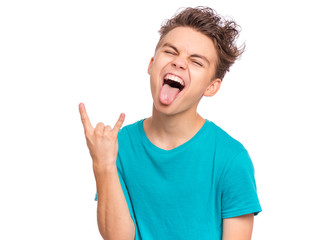Portrait of teen boy making Rock Gesture, isolated on white background. Handsome caucasian young teenager showing horns up gesture. Happy cute child shows tongue and doing heavy metal rock sign. © valiza14