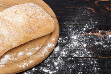 Loaf of ciabatta bread on a cutting board on the dark wooden table