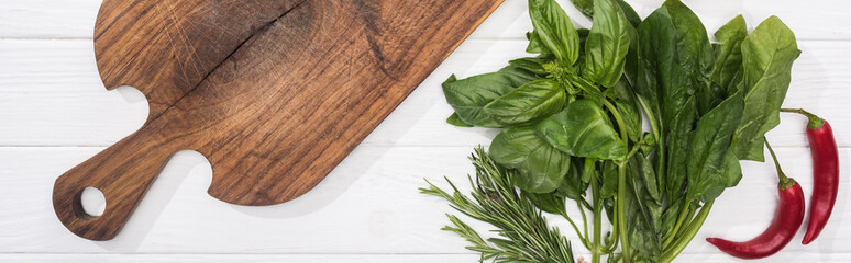 panoramic shot of wooden chopping board, chili peppers and greenery