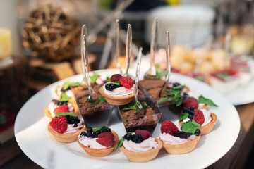 Tasty sweets on a brown rustic wooden banquet table. Summer wedding in the forest. Banquet table. Wedding candy bar. Sweet caces with raspberries, blackberries and mint - 282257736