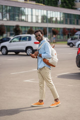 handsome african american man looking at camera while standing on car parking and holding smartphone