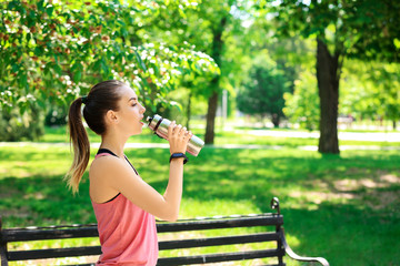 Sporty young woman drinking water after training outdoors