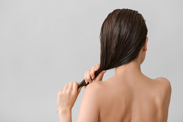 Beautiful young woman after washing hair against grey background, back view