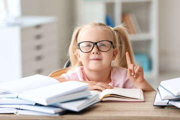 Smart little schoolgirl with raised index finger in classroom