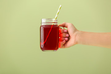 Female hand holding mason jar of fresh pomegranate juice on color background