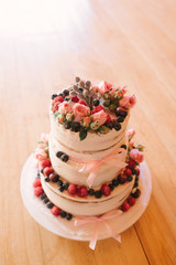 Beautiful white cream wedding cake decorated with fresh strawberries, blueberries and pink roses on wooden background