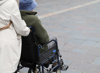 Closeup of elderly disabled woman  in wheelchair assists by female assistant.