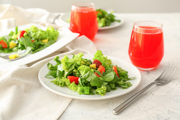 Plates with fresh tasty salad and glasses of juice on table