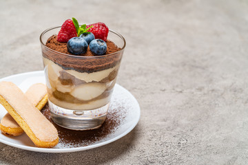 Classic tiramisu dessert with blueberries and raspberries and savoiardi cookies in a glass on concrete background