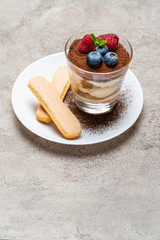 Classic tiramisu dessert with blueberries and raspberries and savoiardi cookies in a glass on concrete background
