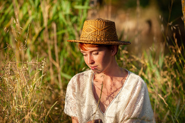 WELLNESS, RELAXATION, WOMAN WITH A STRAW HAT IN THE GRASS IN THE COUNTRYSIDE.