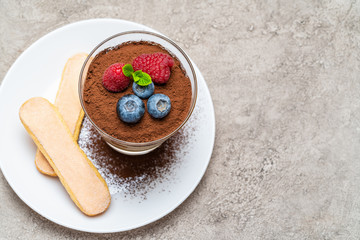 Classic tiramisu dessert with blueberries and raspberries and savoiardi cookies in a glass on concrete background