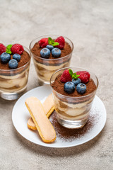 Classic tiramisu dessert with blueberries and raspberries and savoiardi cookies in a glass on concrete background