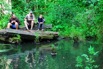 A man with boys fishing on a small river.