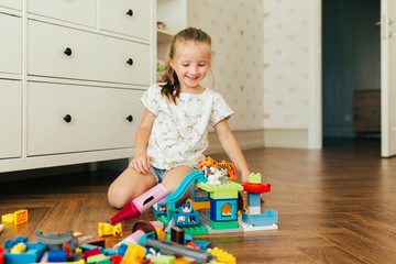 Little girl playing with colorful toy blocks. Educational and creative toys and games for young children. Playtime and mess in kid's room