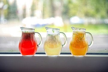 Three types of lemonade in decanters on a windowsill on a street background.