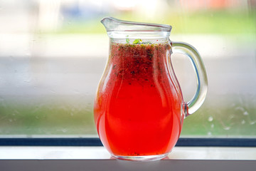Red lemonade in a decanter on a windowsill against a street background.