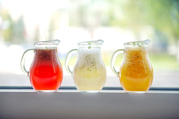 Three types of lemonade in glass decanters on a windowsill on a street background.