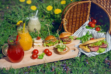 Lemonade in glass decanters and sandwiches during a picnic on the green grass.