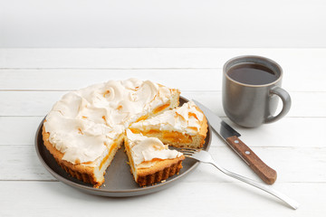 Homemade apricot pie decorated with meringue and a mug of tea on a white wooden table. Copyspace.