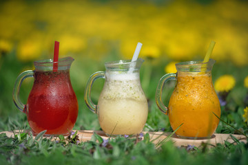 Different color lemonade in glass decanters with drinking straws on the green grass.