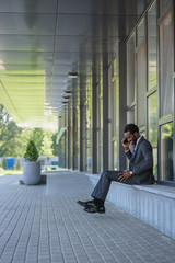 smiling african american businessman talking on smartphone while sitting near office building