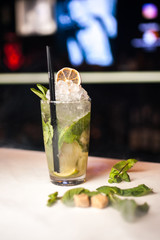 Close-up mojito cocktail with dried lemon and mint on the bar, blurred background.
