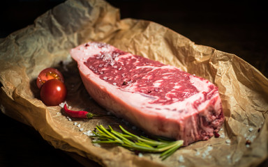 Marbled beef steak on parchment, coarse salt, cherry tomatoes, greens