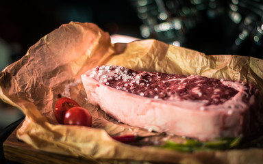 Marbled beef steak on parchment, coarse salt, cherry tomatoes, greens