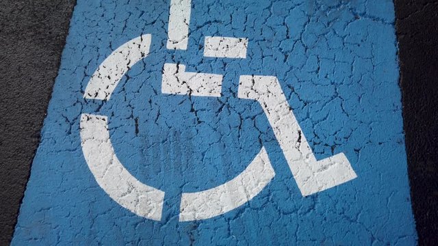 A blue handicapped parking space on pavement in a parking lot, top down view, panning down.