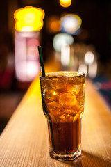 Close-up long island cocktail with lemon on the bar, blurred background.