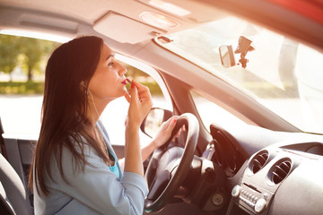 Beautiful woman doing makeup driving her car