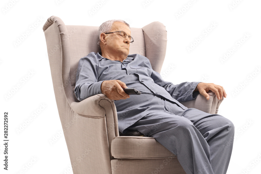 Wall mural elderly man in pyjamas sleeping in an armchair and holding a remote control