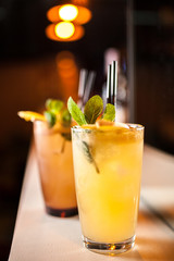 Two orange cocktails with orange and mint on the bar, blurred background.
