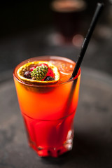 Orange cocktail with spruce cone on dark bar